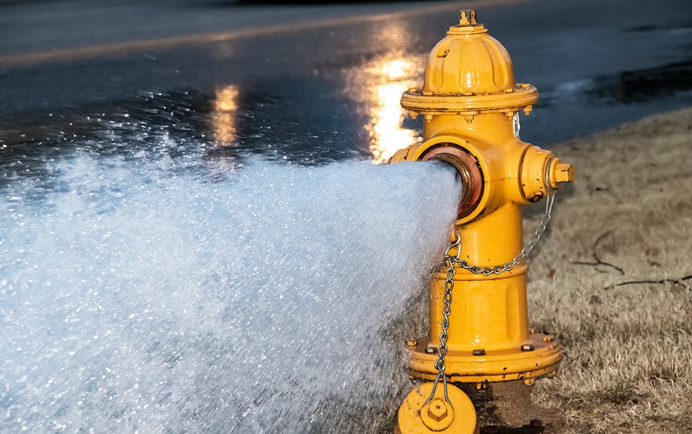 Yellow fire hydrant blasting water at high pressure, flushing the system.