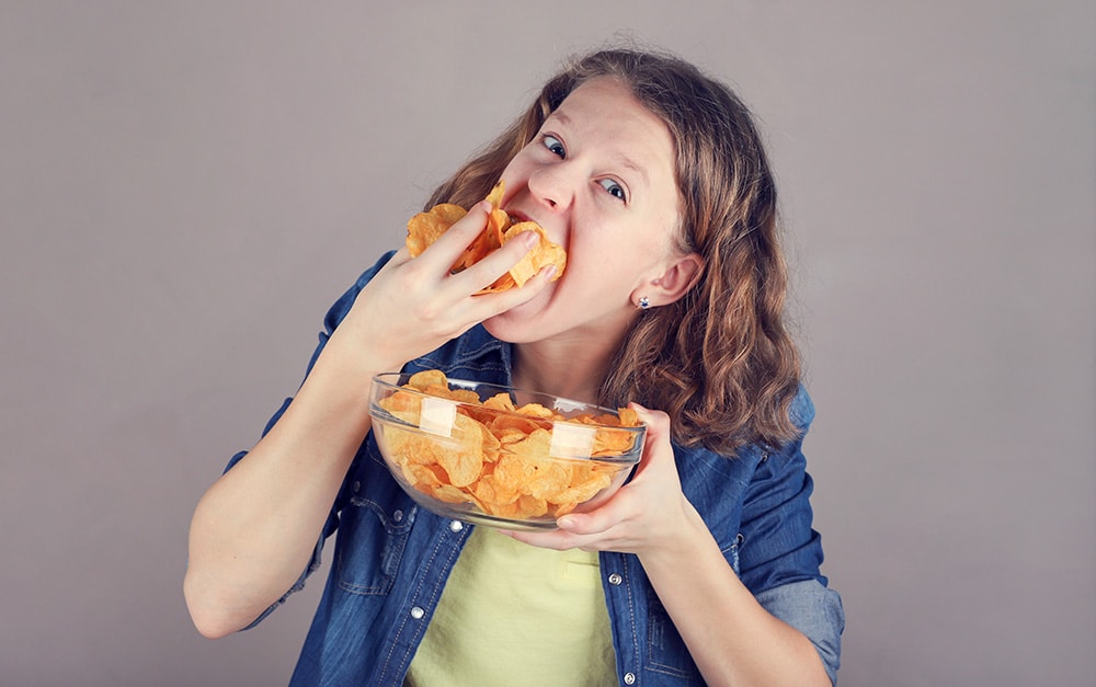 Image of young girl stuffing a handful of potato chips into her mouth.